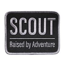 Rektangulärt märke med grå langetterad kant och svart bakgrund med texten SCOUT Raised by Adventure på